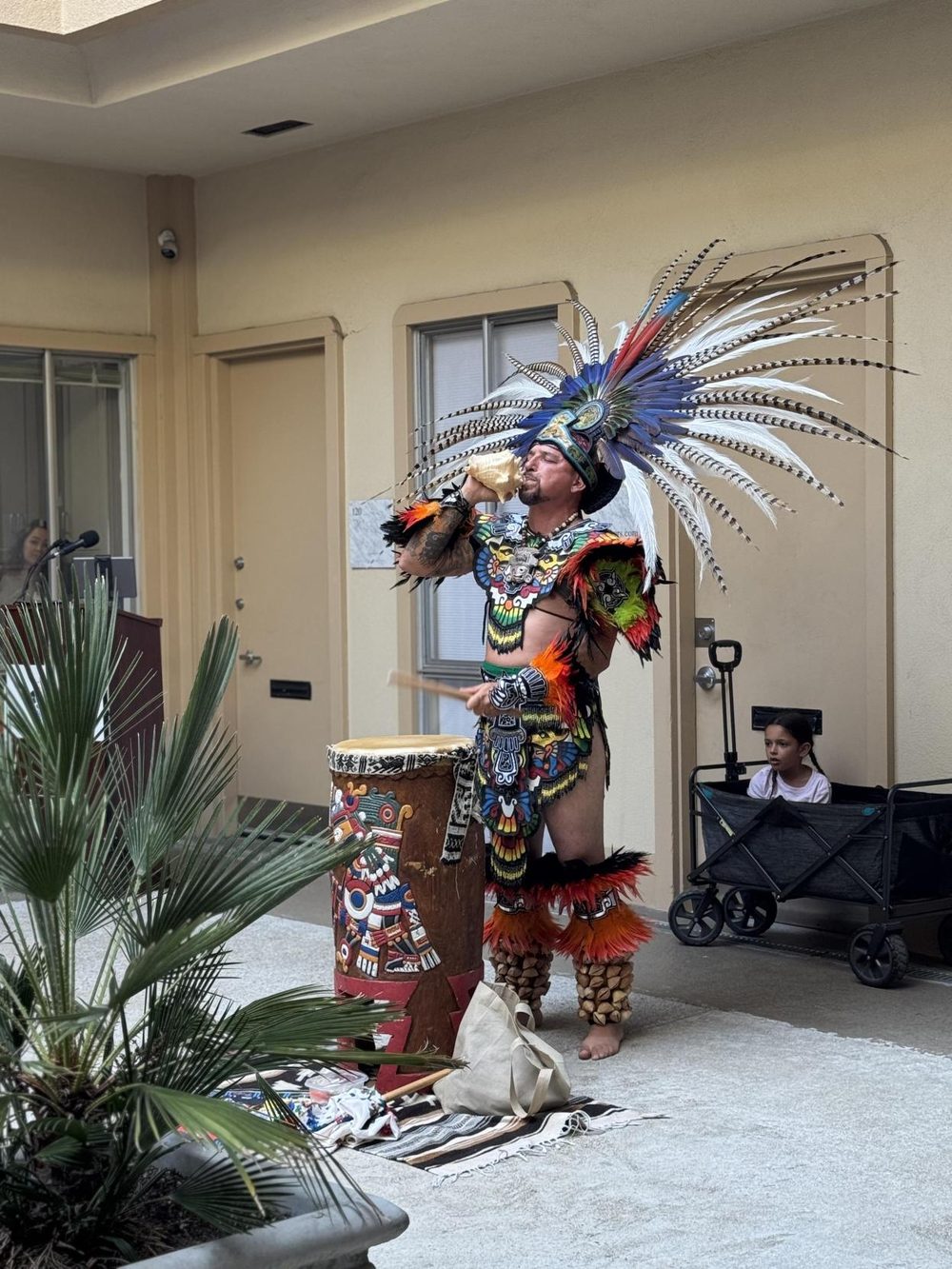 A Danza Azteca musician playing a conch shell beside a traditional drum